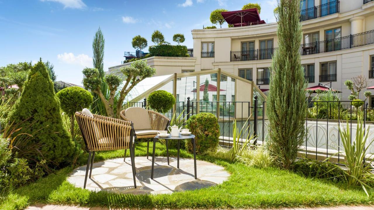 Cvk Park Bosphorus Hotel Istanbul Exterior photo The photo features a small outdoor seating area with two stylish chairs and a round table set on a stone patio. The setting is surrounded by well-maintained grass and decorative plants, creating a serene atmosphere. In the background, a modern buildi