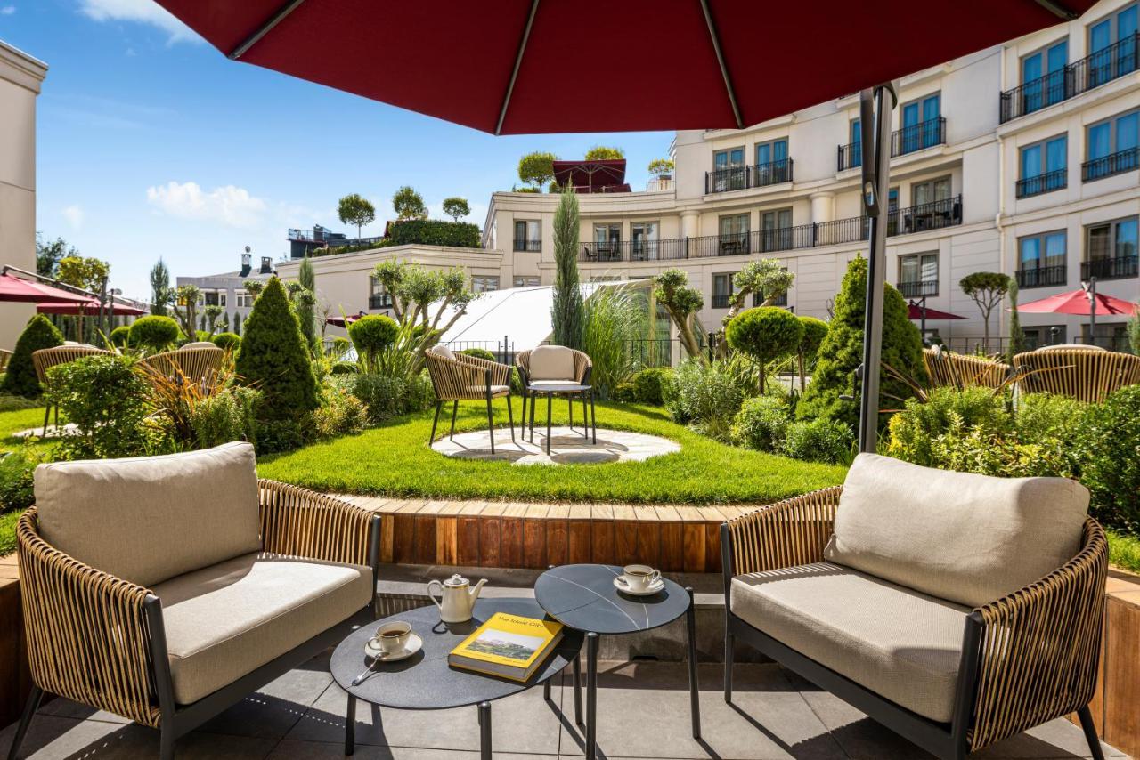 Cvk Park Bosphorus Hotel Istanbul Exterior photo The photo shows a beautifully designed outdoor lounge area. There are two comfortable chairs with light cushions positioned around small tables. On the tables, there are coffee cups and a book, suggesting a cozy atmosphere. In the background, there i