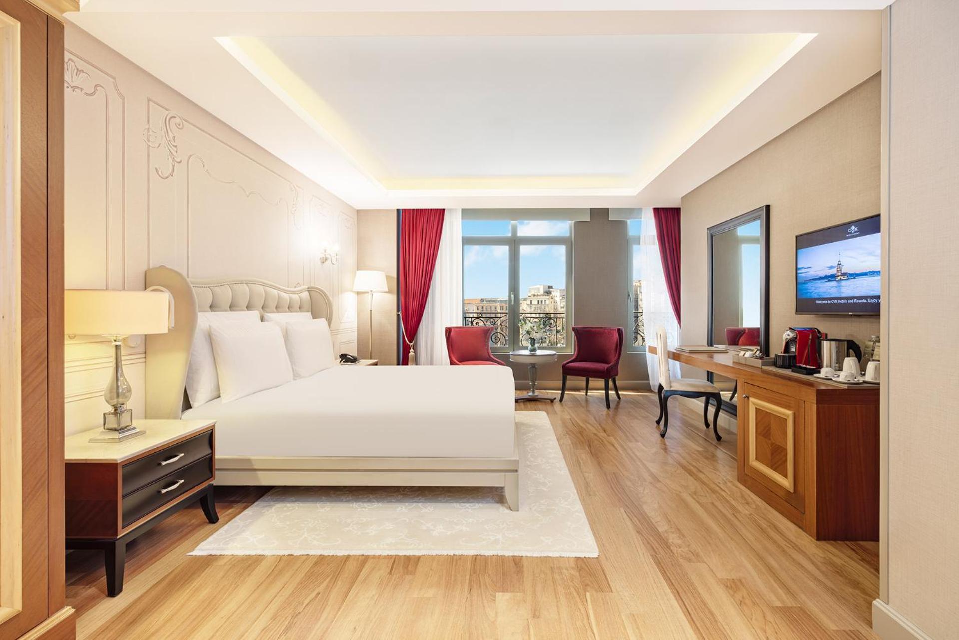 Cvk Park Bosphorus Hotel Istanbul Exterior photo The photo shows a modern hotel room. It features a large bed with white linens, flanked by bedside tables with lamps. The walls have a light, neutral color with decorative molding, while large windows are dressed with red curtains that let in natural