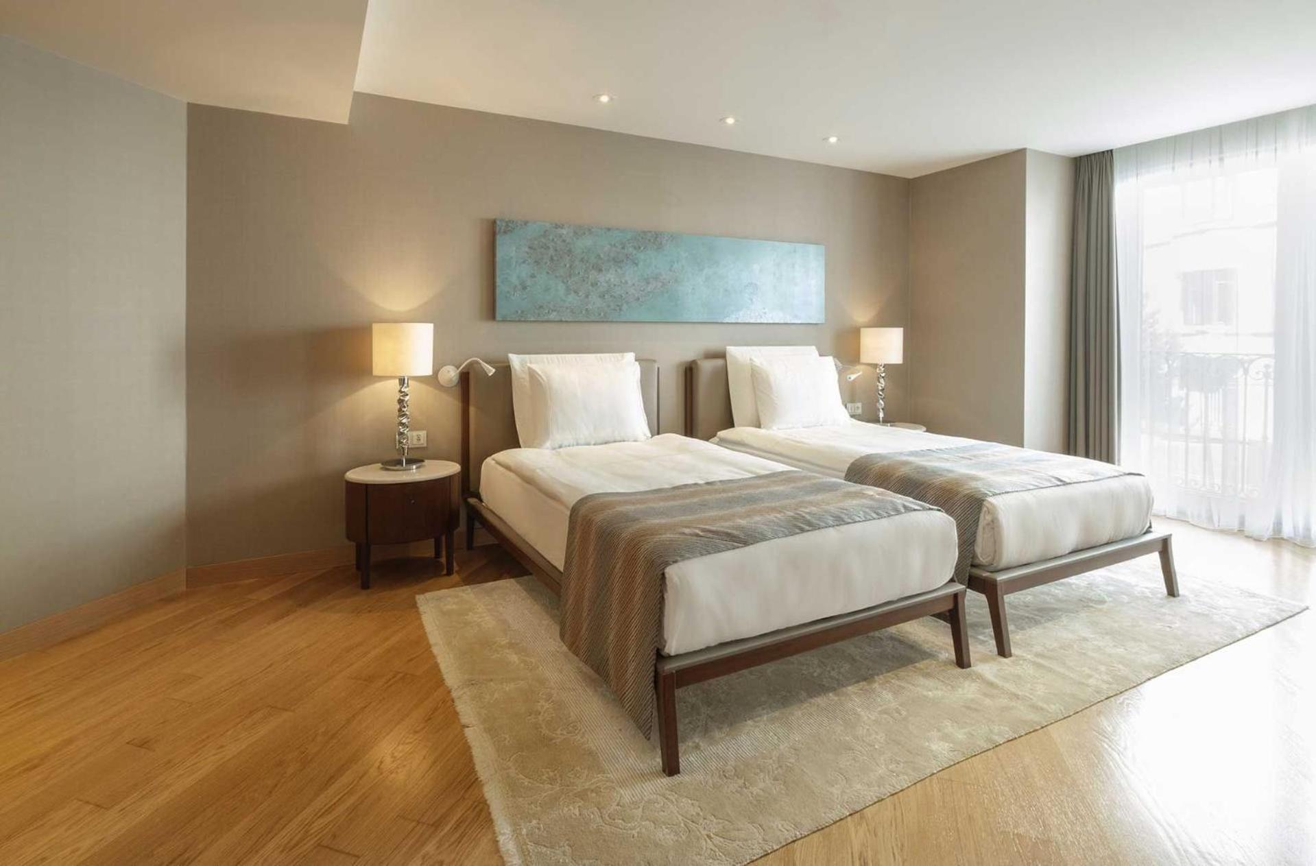 Cvk Park Bosphorus Hotel Istanbul Exterior photo The photo shows a modern hotel room featuring two single beds placed side by side. Each bed is dressed in white linens with a light gray and brown striped bed runner. There are bedside tables with lamps on each side of the beds. The room has wooden f