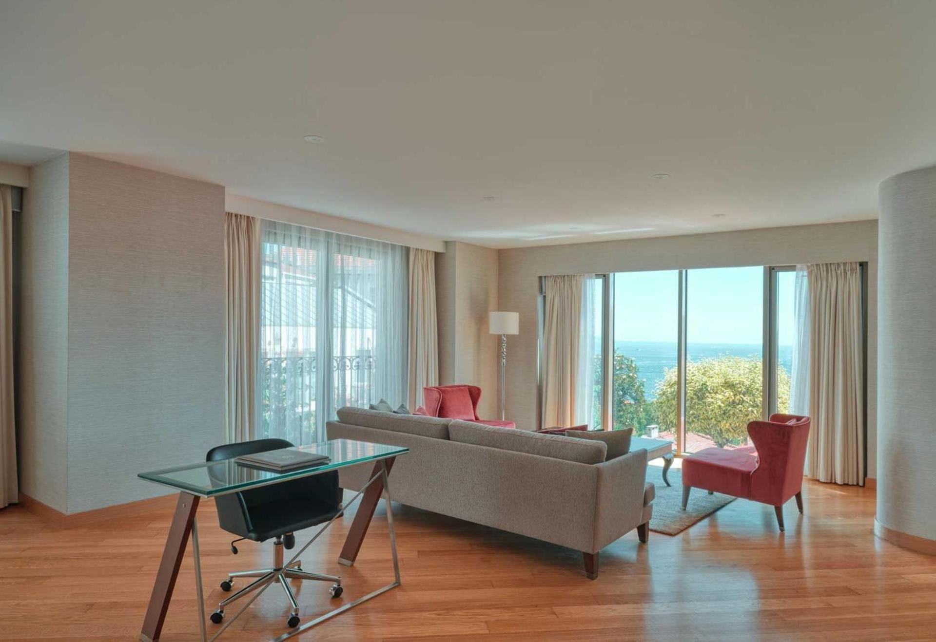 Cvk Park Bosphorus Hotel Istanbul Exterior photo The photo shows a modern living space with large windows offering a view of the outdoors. The room features a light-colored, minimalist design with hardwood flooring. There is a gray sofa with pink cushions, and a pink armchair nearby. A glass-top ta