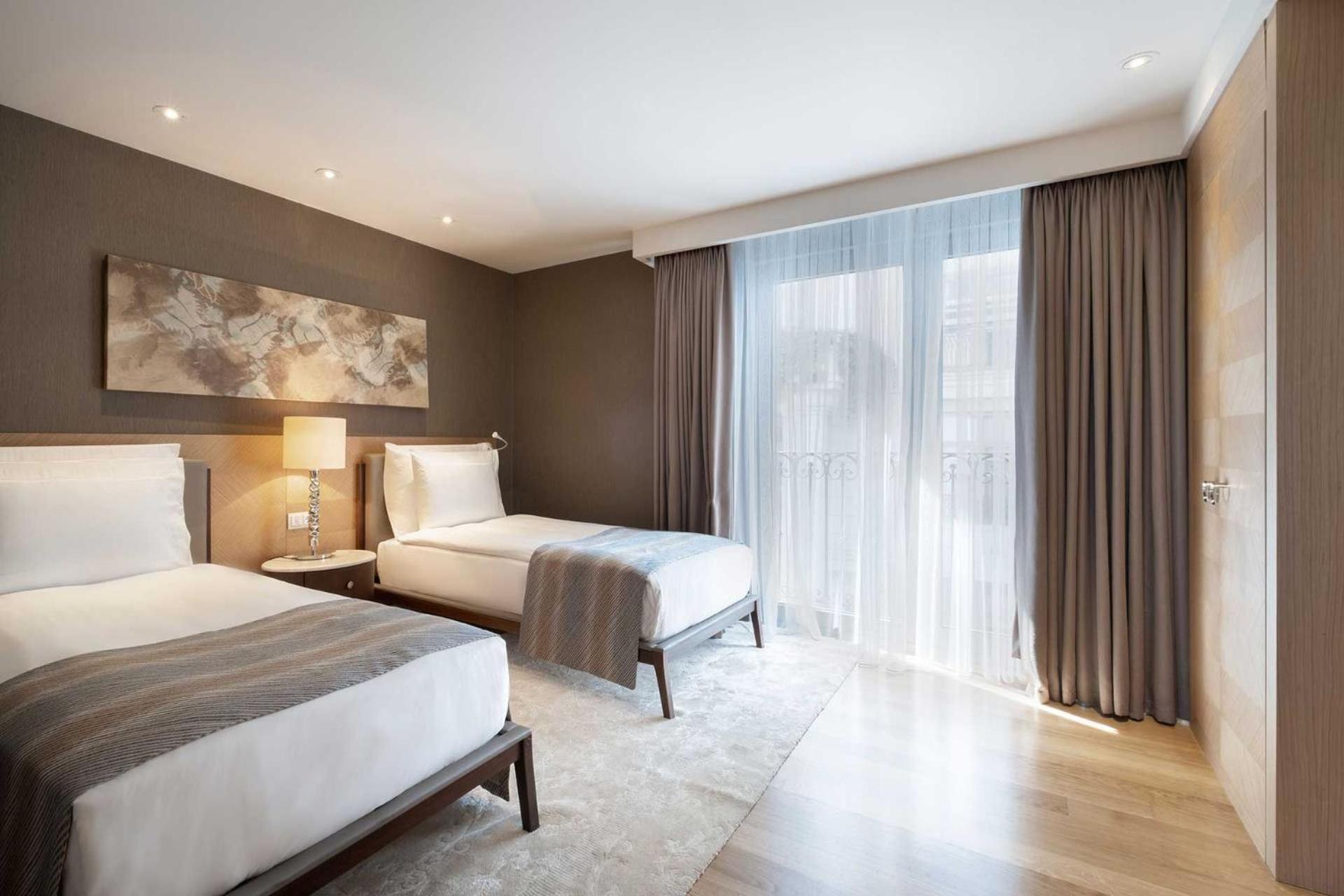 Cvk Park Bosphorus Hotel Istanbul Exterior photo The photo shows a modern hotel room featuring two twin beds with crisp white bedding and light gray throw blankets. The walls have a warm brown tone, and there's a large window draped with sheer curtains, allowing natural light to fill the room. A pi