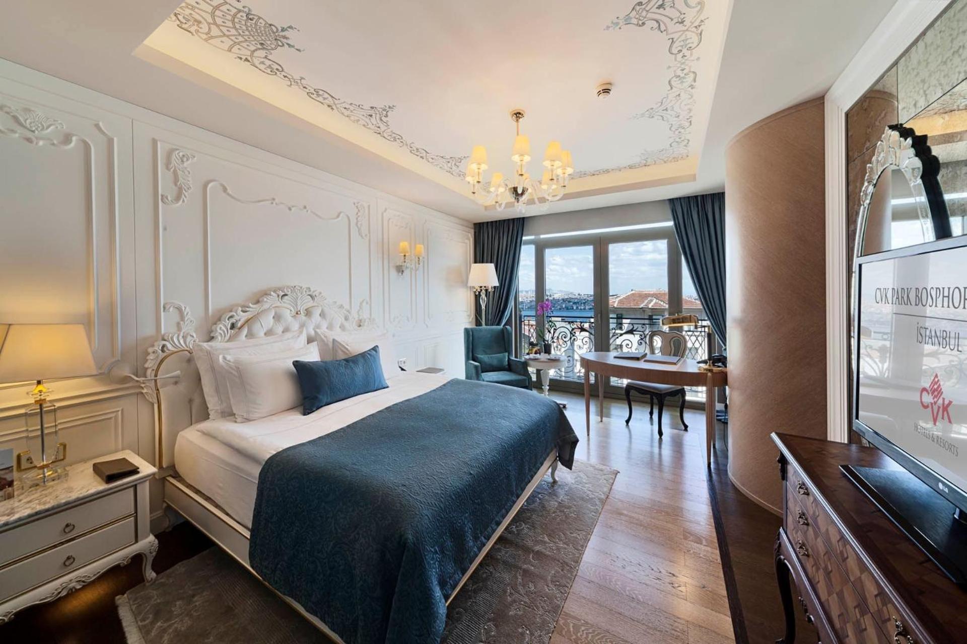 Cvk Park Bosphorus Hotel Istanbul Exterior photo The photo shows a luxurious hotel room designed in an elegant style. It features a large bed with a white frame, adorned with decorative molding on the headboard and topped with a blue blanket and decorative pillows. The room has a sophisticated chan