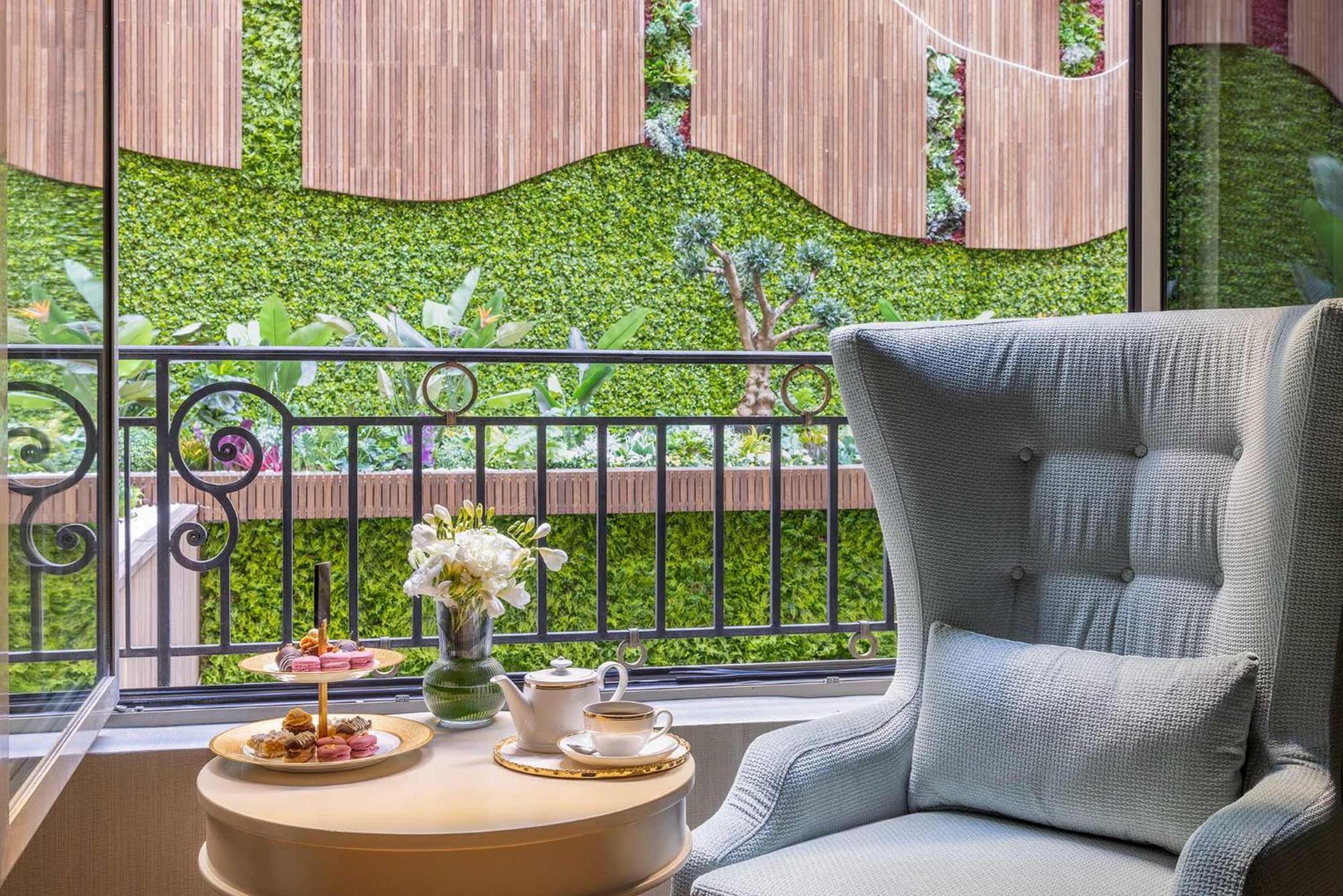 Cvk Park Bosphorus Hotel Istanbul Exterior photo The photo shows a cozy interior setting featuring a comfortable, light blue armchair. In front of the chair, there is a small table with a teacup, a plate of pastries, and a vase with fresh flowers. Behind the chair, large windows provide a view of a