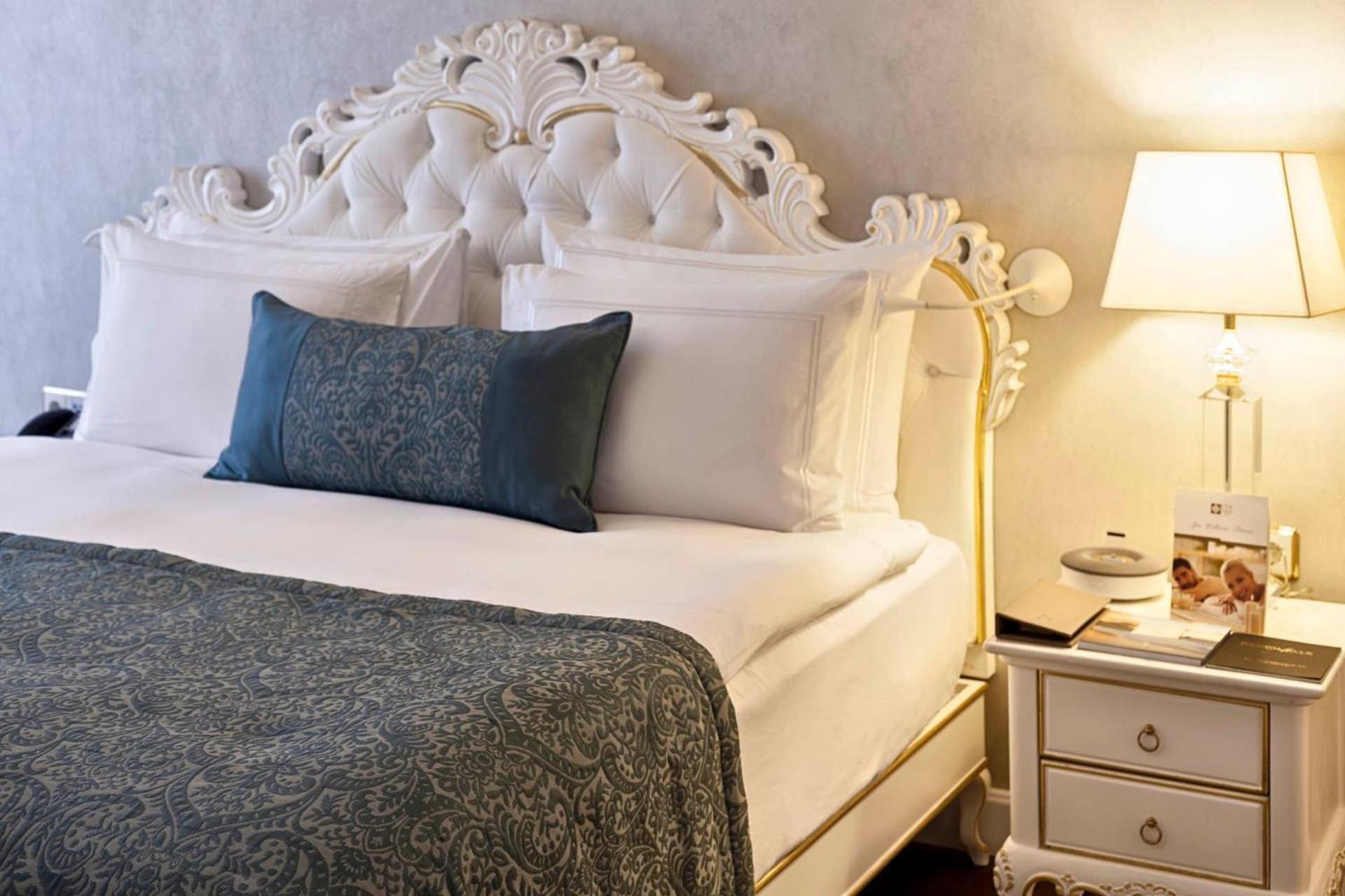 Cvk Park Bosphorus Hotel Istanbul Exterior photo The photo depicts a luxurious bedroom setting. It features an elegant bed with an ornate white headboard and plush white bedding. There is a decorative blue throw pillow on the bed, adding a pop of color. To the side, there's a bedside table with a s
