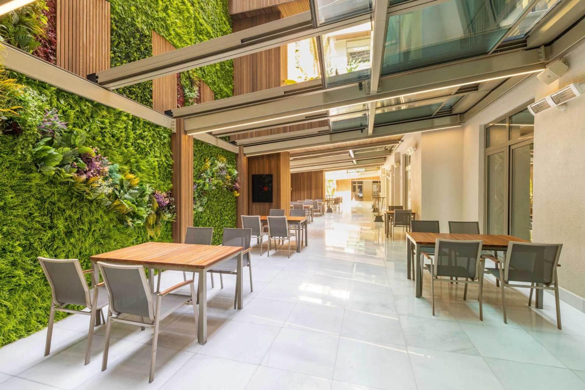 Cvk Park Bosphorus Hotel Istanbul Exterior photo The photo shows a modern, well-lit interior space that features a green wall filled with plants on one side. There are several wooden tables and chairs arranged neatly, suggesting it could be an area for dining or socializing. The overall design is s