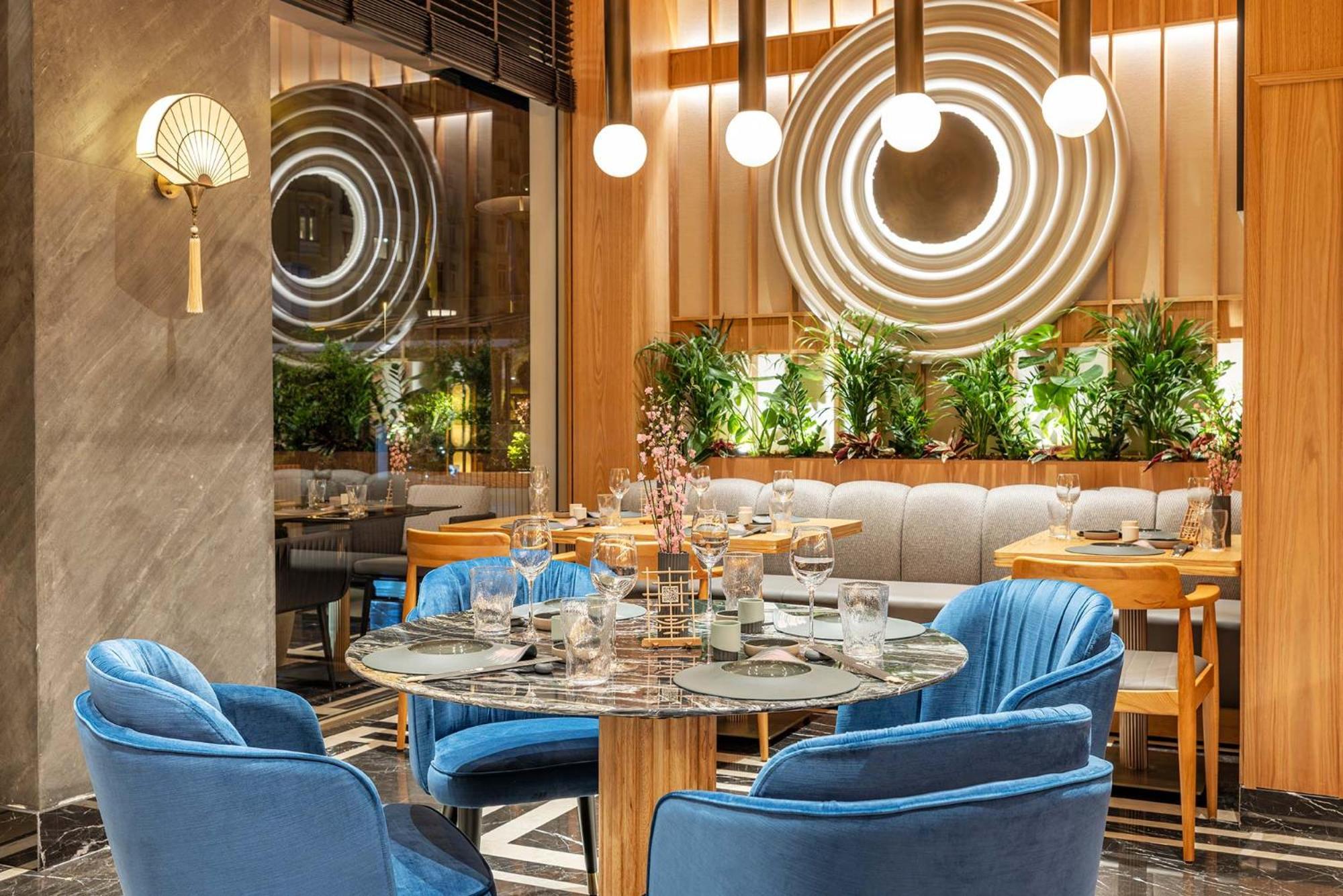 Cvk Park Bosphorus Hotel Istanbul Exterior photo The photo depicts a stylish and modern dining area in a restaurant. There is a circular table surrounded by plush blue chairs. The table is set with glassware, suggesting readiness for dining. In the background, there's a cozy banquette seating arran