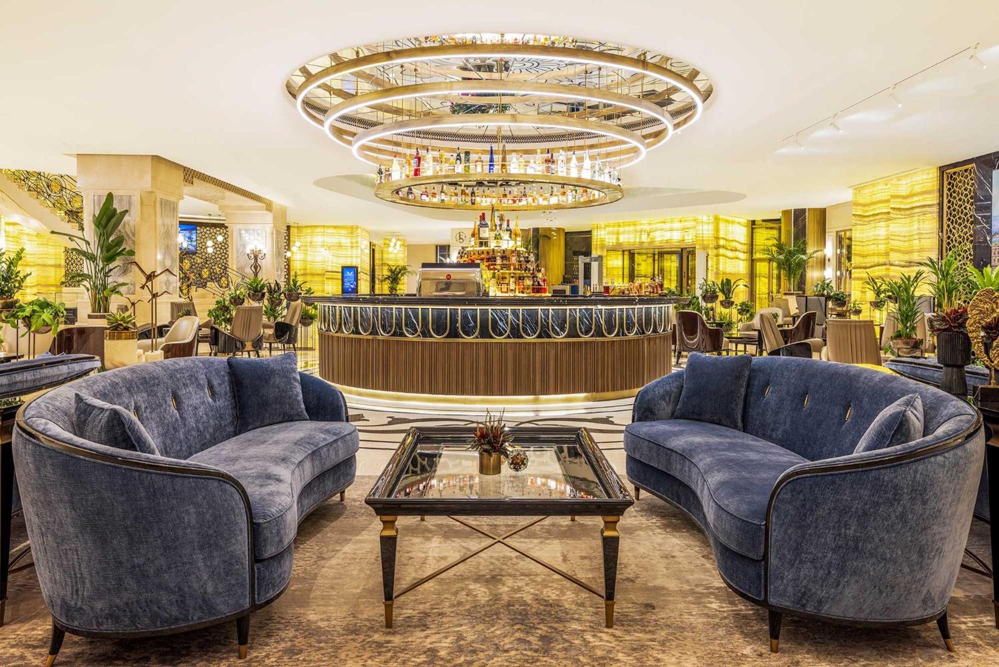 Cvk Park Bosphorus Hotel Istanbul Exterior photo The photo shows a luxurious hotel lobby or lounge area. In the center, there is a stylish bar with a curved counter, illuminated by a striking chandelier above it. The space features elegant decor, with soft blue sofas arranged around a glass-topped 