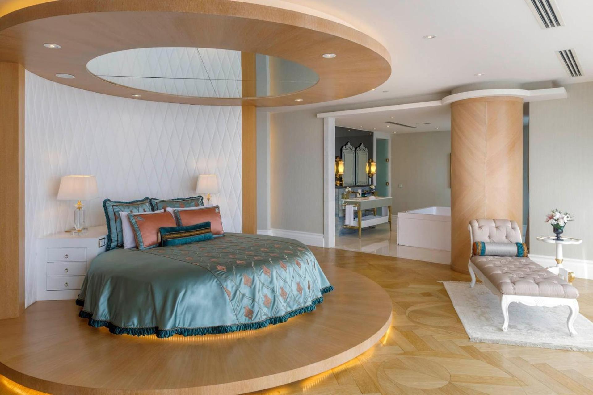 Cvk Park Bosphorus Hotel Istanbul Exterior photo The photo shows a luxurious bedroom featuring a circular bed positioned on a raised platform. The bed is adorned with a teal-colored bedspread and decorative pillows. There is a stylish armchair nearby and a bedside table with a lamp. In the backgrou